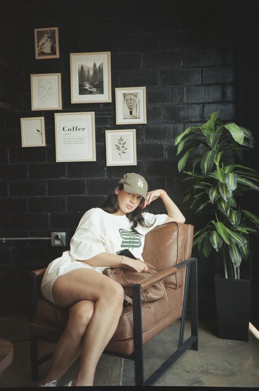 Natasha Valentina seated in a cafe beside framed art and a plant