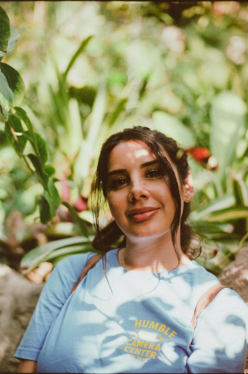 Natasha Valentina in a sunlit garden wearing a blue T-shirt